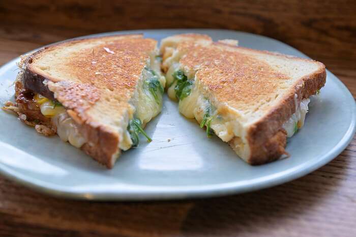 The breakfast grilled cheese sandwich made with cheddar, gruyere, and gouda, bacon tomato jam, arugula, and an over-easy egg on classic sourdough at Hearth & Hug Bakery in Somerville.